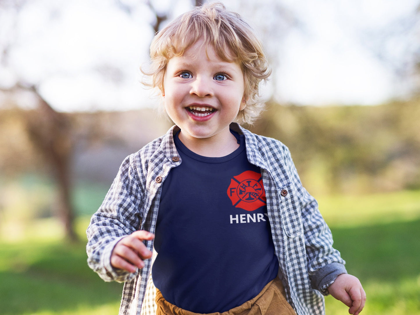 Toddler wearing the personalized firefighter baby bodysuit under a plaid shirt, showing the red Maltese Cross and custom name