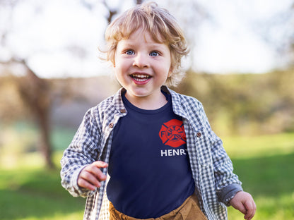 Toddler wearing the personalized firefighter baby bodysuit under a plaid shirt, showing the red Maltese Cross and custom name