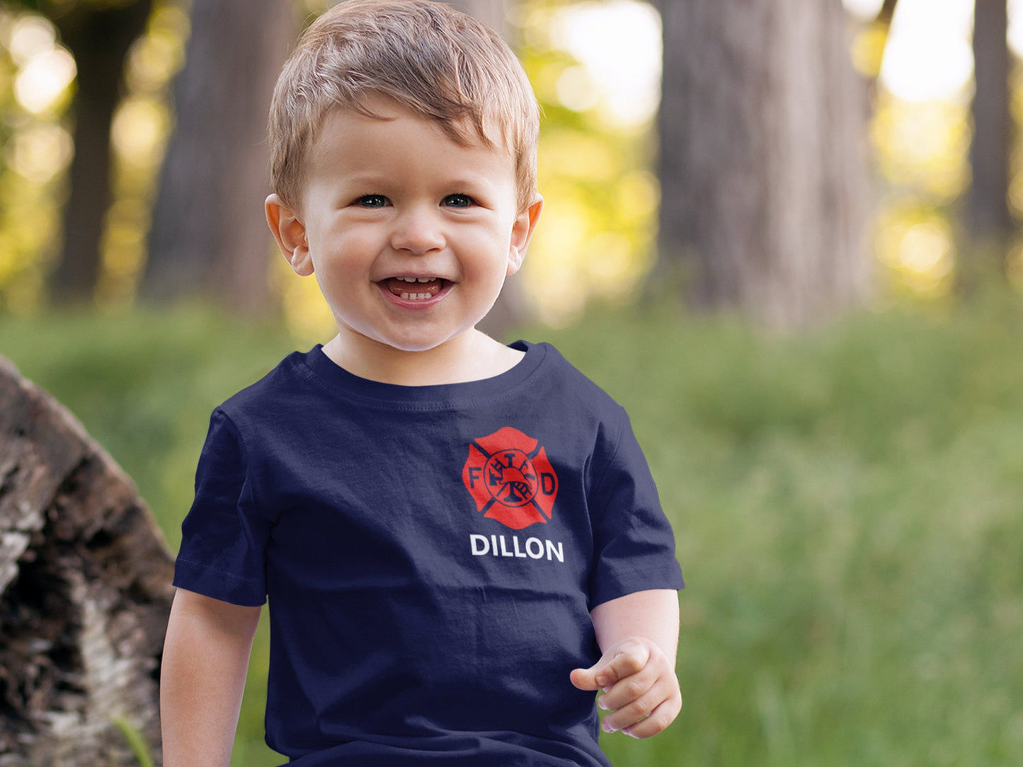 Happy toddler wearing a navy blue shirt with red Maltese cross on left chest and name underneath in white.