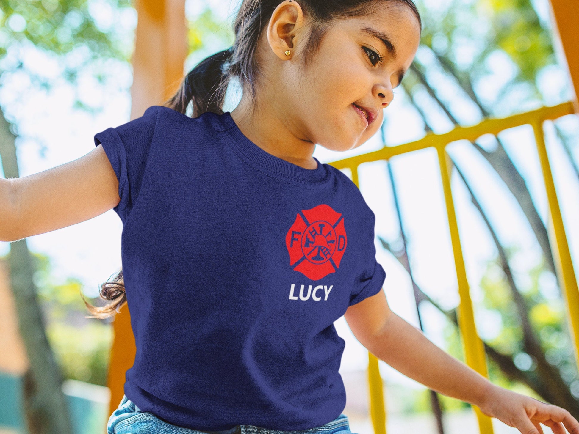 Young girl at playground wearing a navy blue t-shirt with red Maltese cross and her name Lucy underneath.