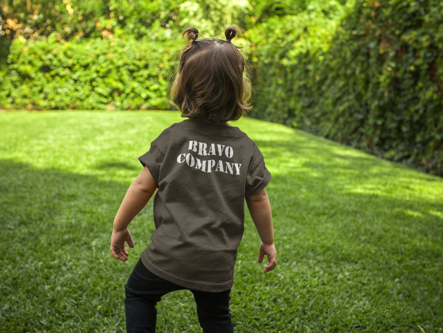 A small child wearing a military green t-shirt with the words 'BRAVO COMPANY' printed in white on the back.
