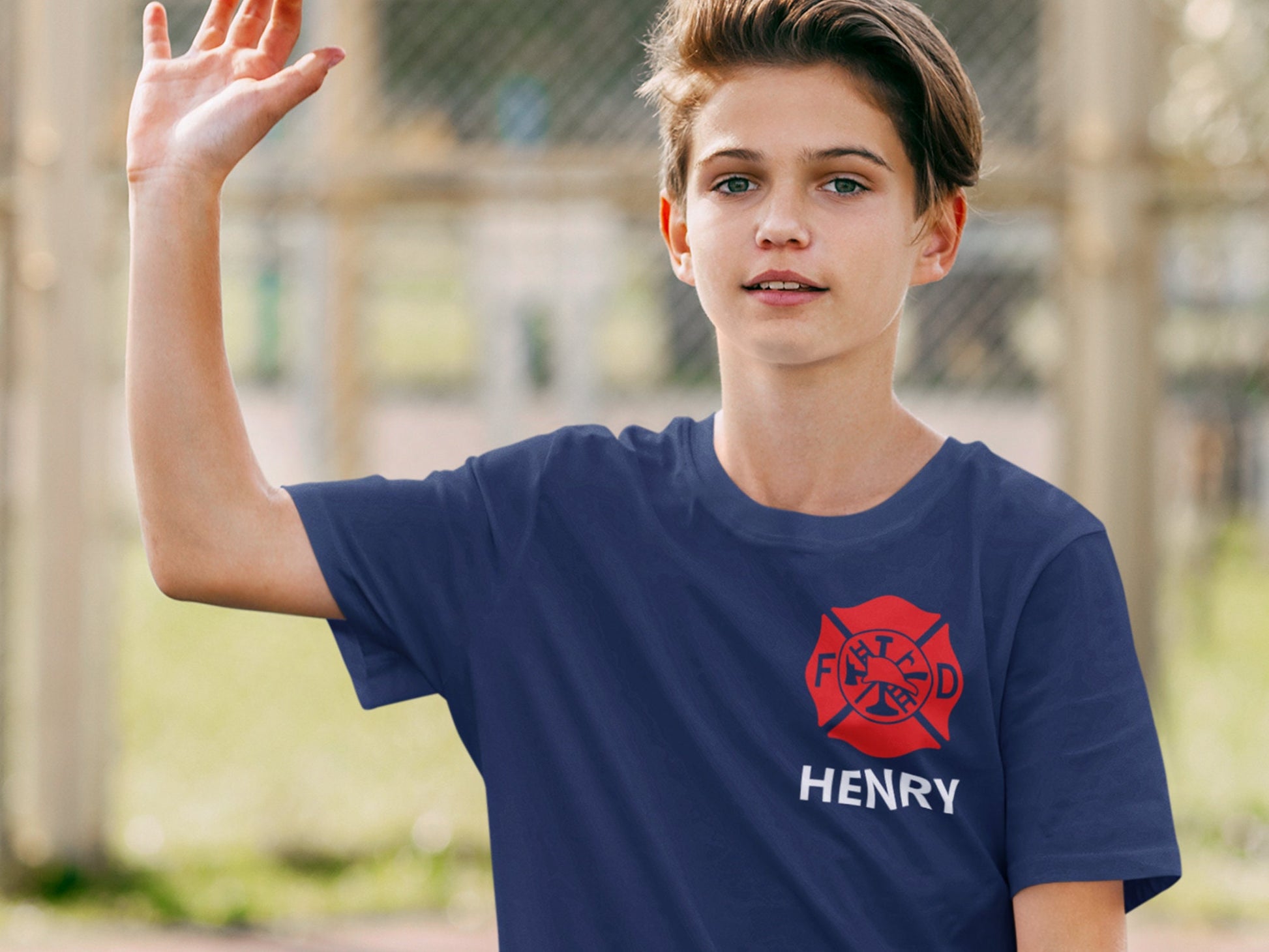 Teen boy with hand raised wearing a navy blue T-shirt with red Maltese cross and the name Henry underneath.
