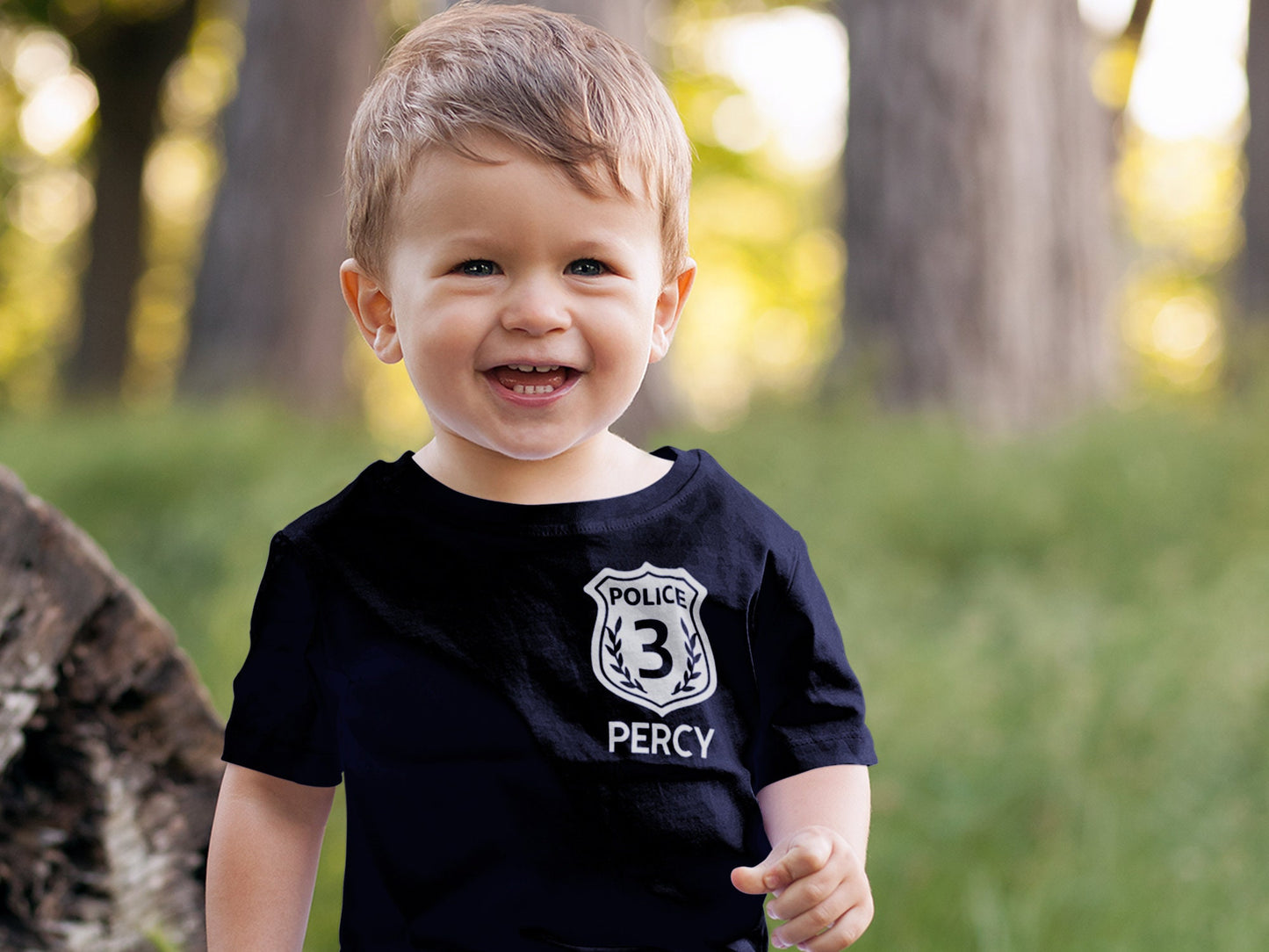 Happy toddler wearing a black short sleeve t-shirt with silver police badge with number 3, on left chest with name underneath in silver.
