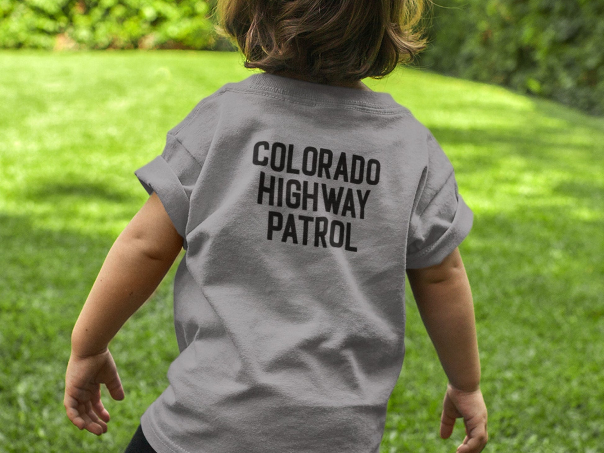 Back view of toddler wearing a gray t-shirt with black text that reads 'COLORADO HIGHWAY PATROL'.