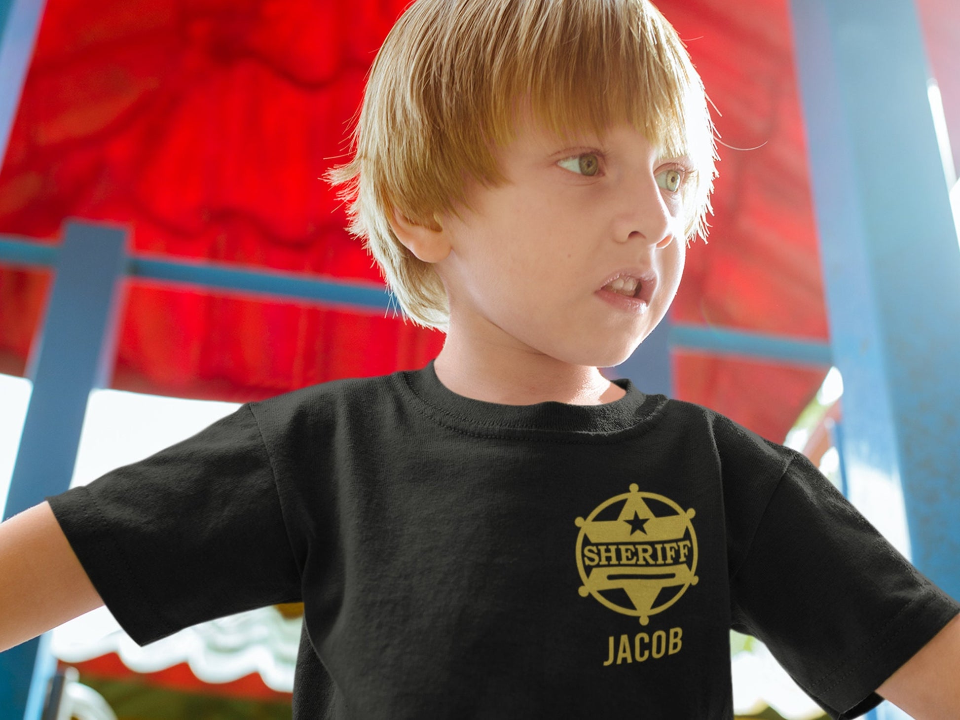 Young boy at playground wearing a short sleeve black t-shirt with gold Sheriff's badge on left chest and his name, Jacob, underneath.