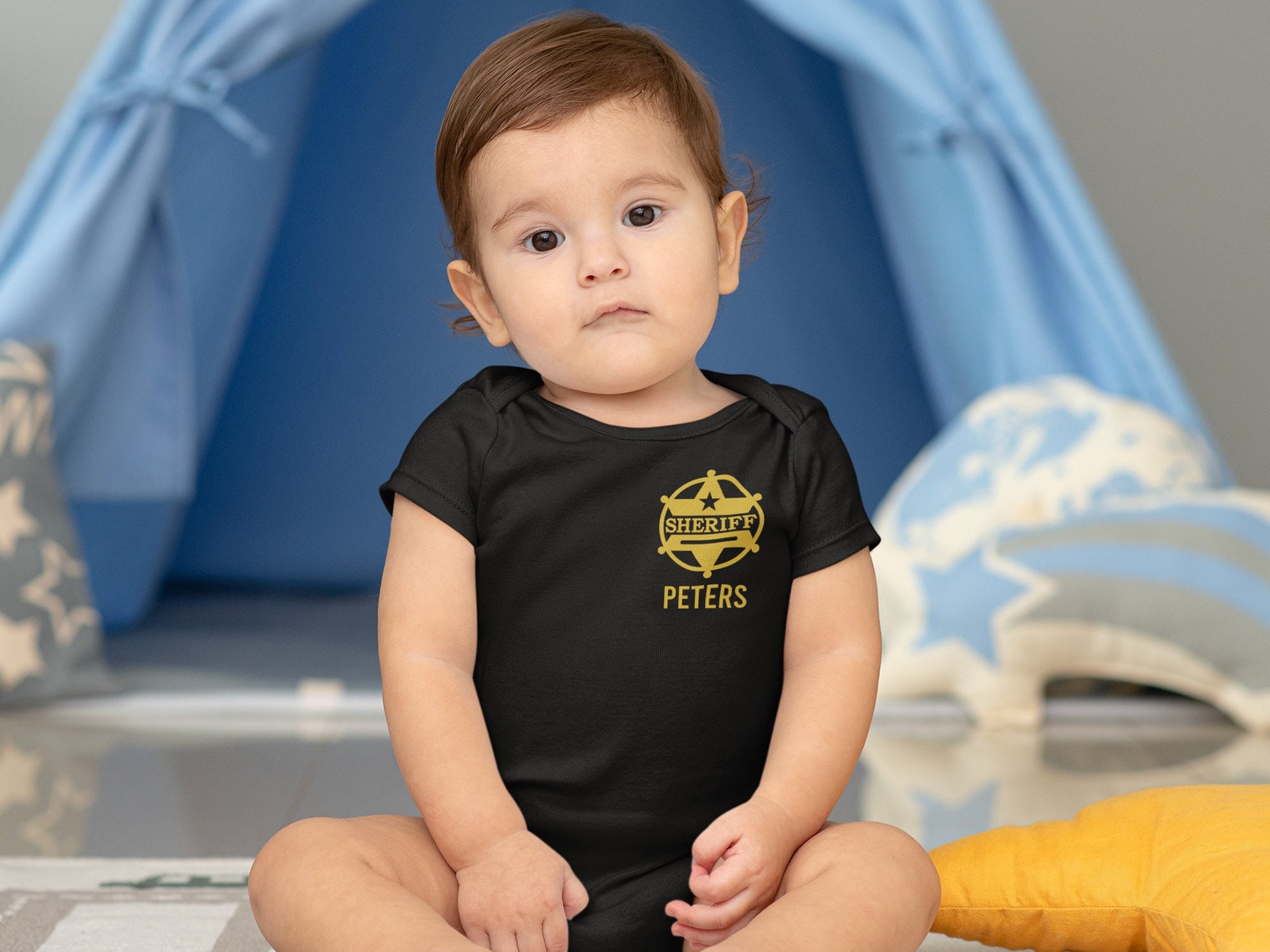 Sitting baby wearing a black s short sleeve bodysuit with a gold sheriff badge on left chest and personalized name underneath.
