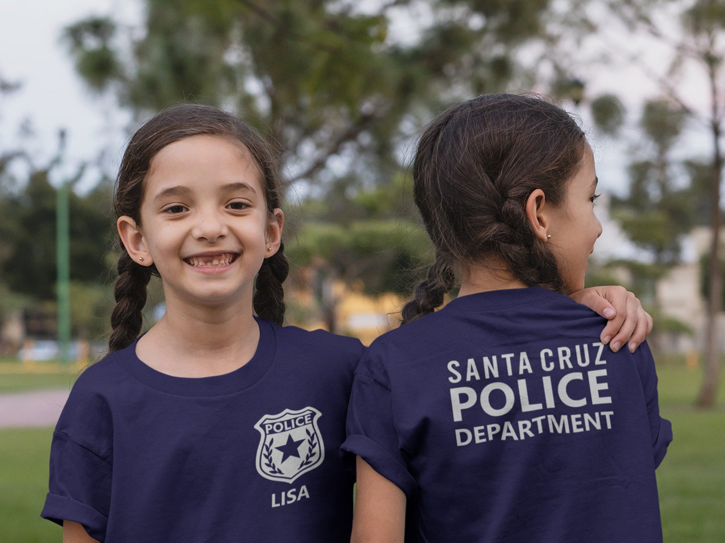A child wearing a navy blue t-shirt with a silver police badge and the name 'LISA' printed on the front. Another child showing back of the shirt has the text 'SANTA CRUZ POLICE DEPARTMENT' printed in silver.