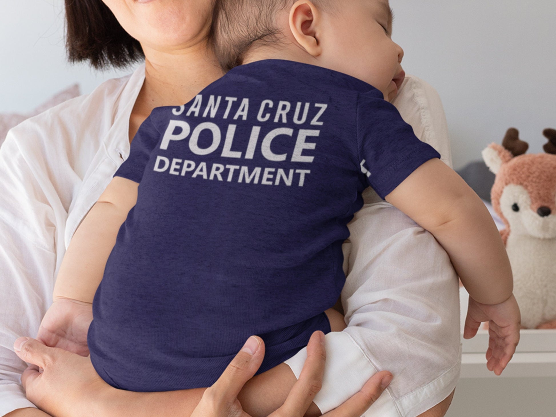 Mom holding a baby on her shoulder. Baby is wearing a navy blue short sleeve bodysuit with silver text “Santa Cruz Police Department” indicating personalization.