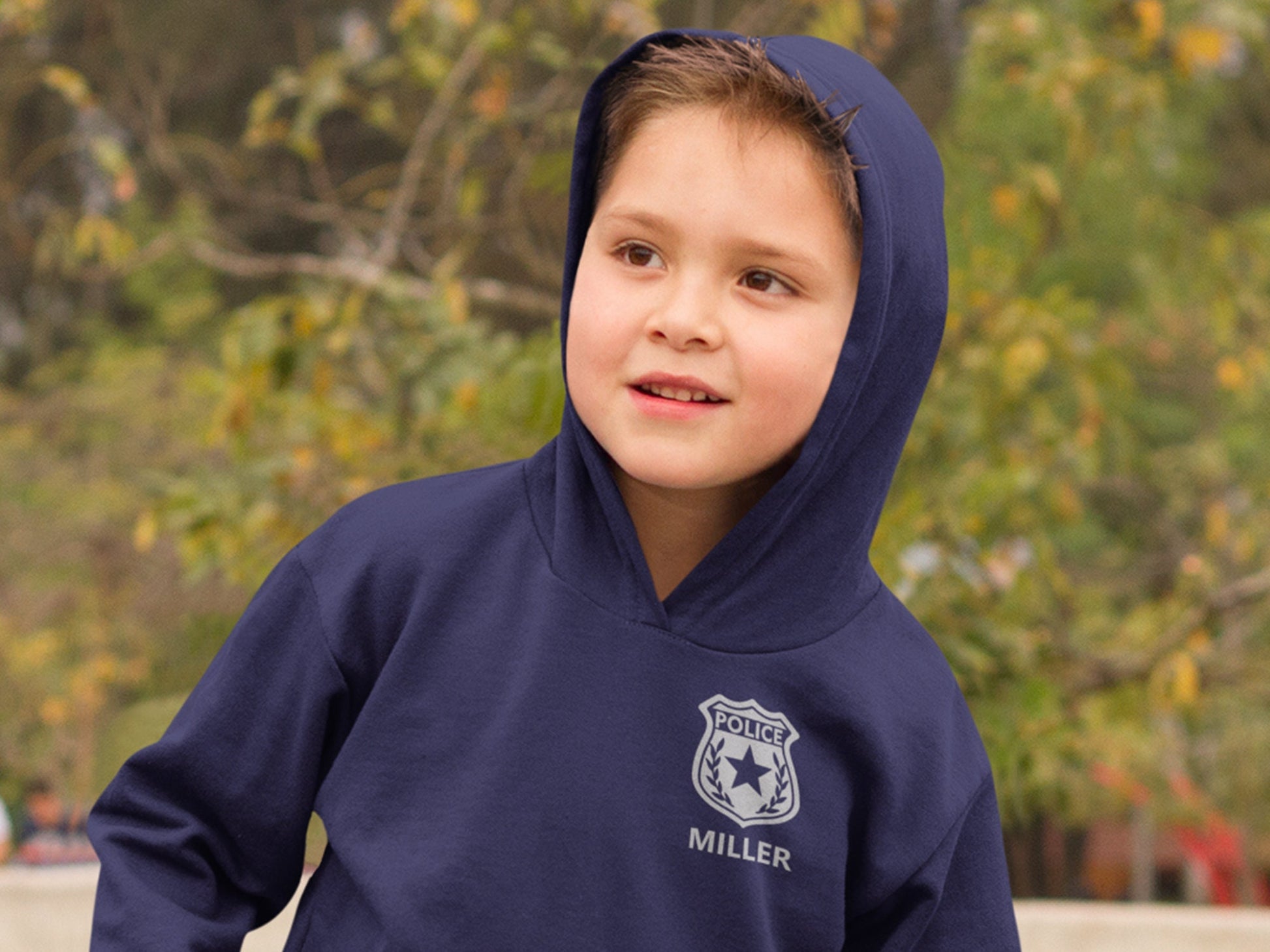 Small boy wearing a navy blue hooded sweatshirt with a silver police badge design and the text 'POLICE' with 'MILLER' underneath in silver text.