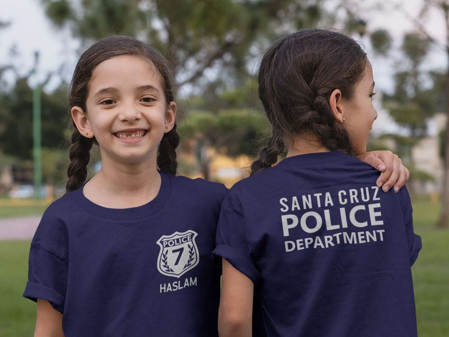 A navy blue t-shirt with silver text and a silver badge. The text on the back of the shirt reads 'Santa Cruz Police Department.' The badge on the front of the shirt has the word 'Police' and the number '7' inside of it. The text 'Haslam' is below the badge.