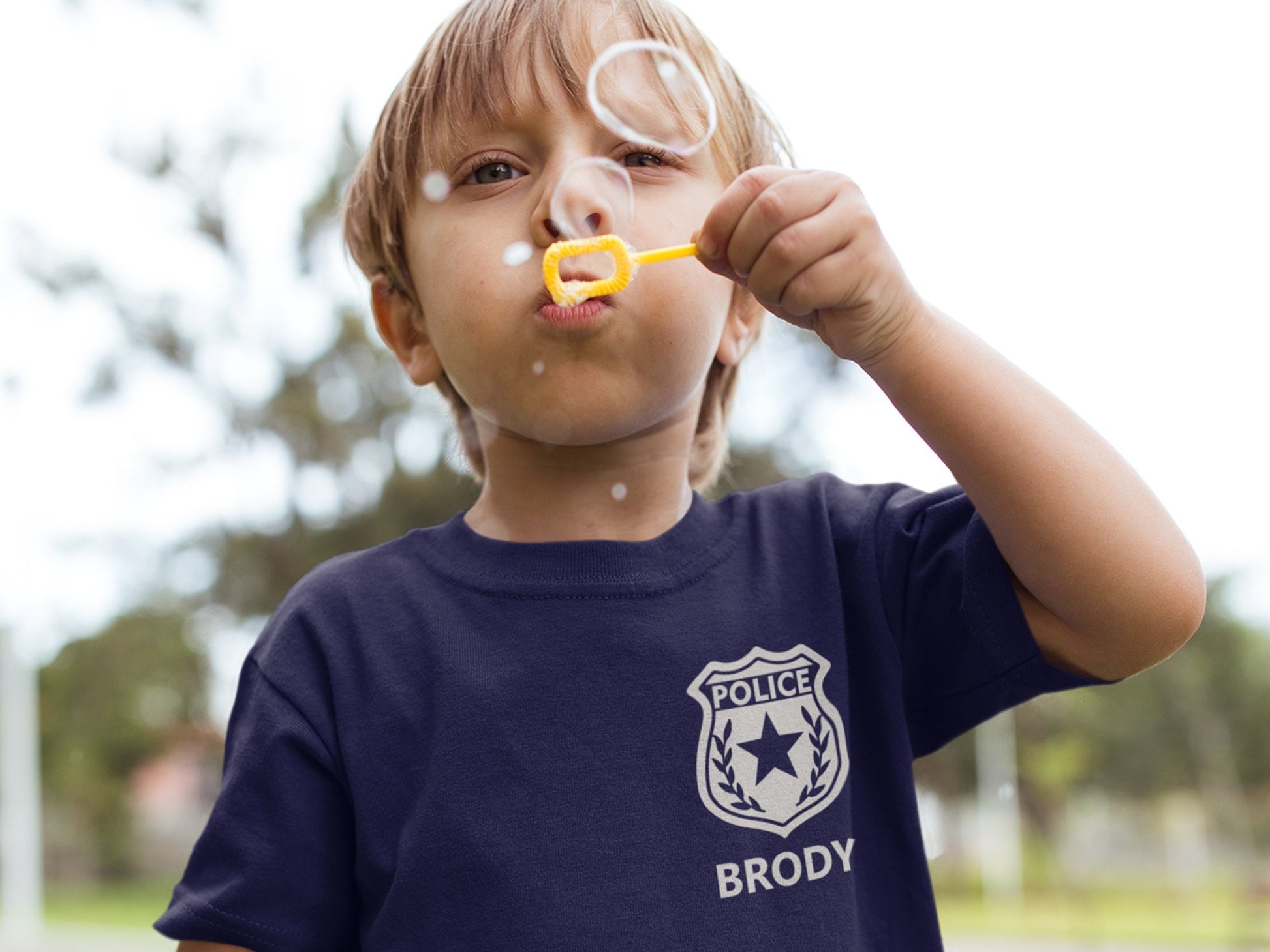 A navy blue t-shirt with a silver police badge design. The badge has a star and laurel wreath. The text 'POLICE' and 'BRODY' are printed on the shirt.