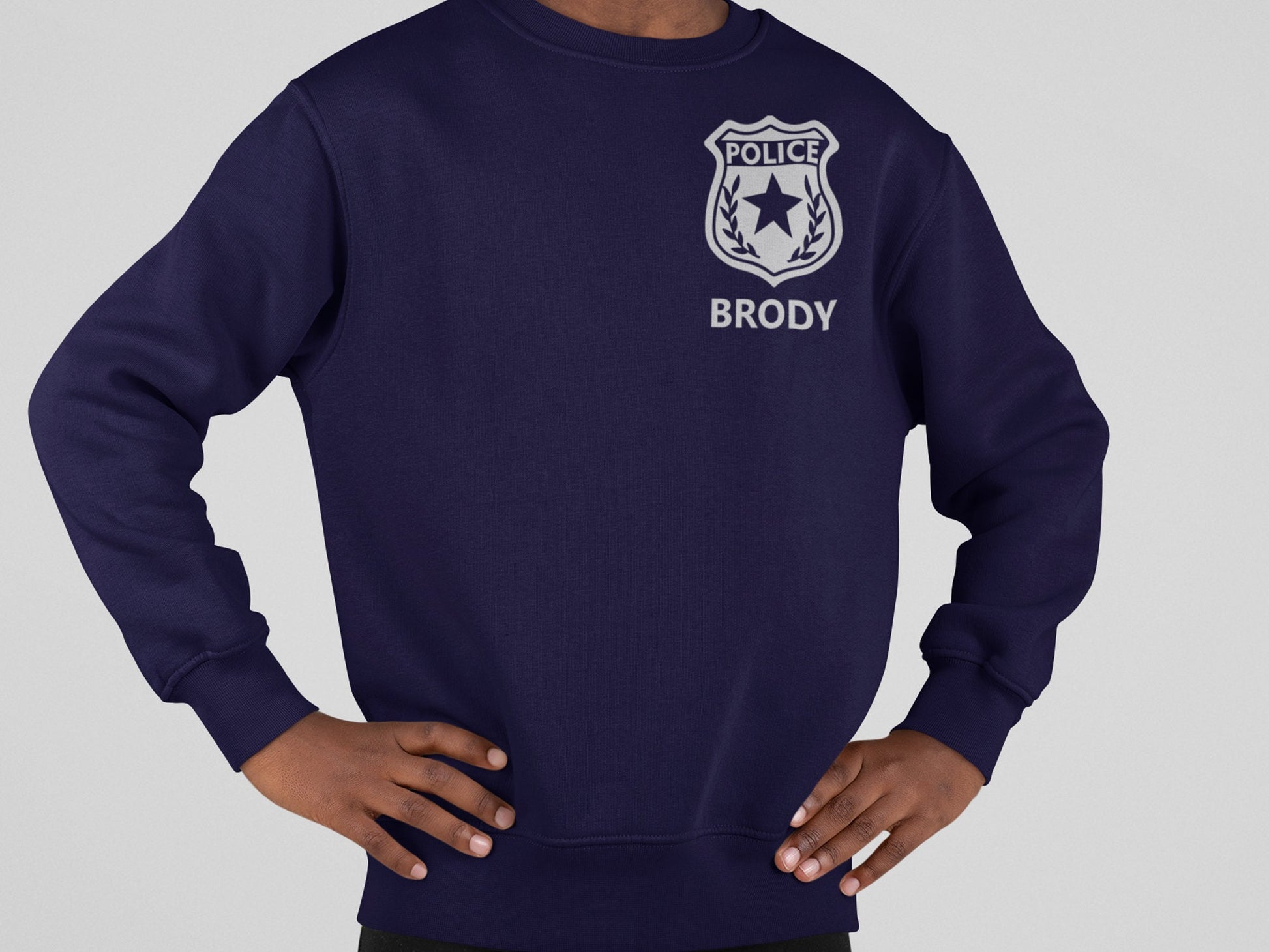 A navy blue sweatshirt with a silver police badge design and the text 'POLICE' with 'BRODY' written underneath in silver text.