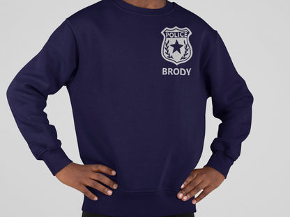 A navy blue sweatshirt with a silver police badge design and the text 'POLICE' with 'BRODY' written underneath in silver text.