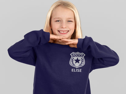 Girl wearing a navy blue sweatshirt with a silver police badge design and the name 'Elise' printed below it in silver.