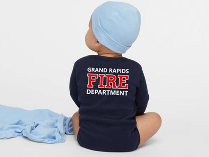 Baby sitting facing backwards wearing a navy blue bodysuit with Grand Rapids Fire department in red and white text.