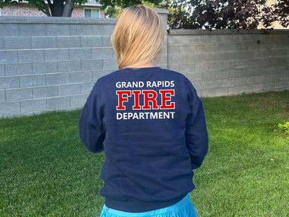 Back view of a girl wearing a navy blue sweatshirt with the words 'Grand Rapids Fire Department' printed on the back in white with the word 'Fire' in red.