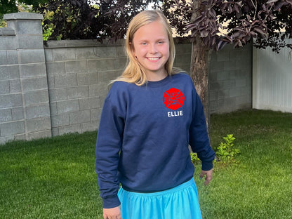 Girl wearing a navy blue sweatshirt with a red firefighter logo on left chest and the name 'ELLIE' printed on the front.