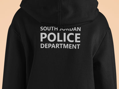 Black hooded sweatshirt with South Jordan Police Department text in white print on the back. The text is stacked vertically with 'SOUTH JORDAN' at the top, 'POLICE' in a larger font in the middle, and 'DEPARTMENT' at the bottom.  The hoodie is a dark, solid color with a drawstring hood.