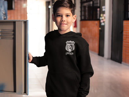 Black child-size hoodie sweatshirt with a white police badge graphic. The badge features the text 'POLICE' above the number '12' and 'WATSON' below.  The hoodie has a drawstring hood and kangaroo pocket. The sweatshirt is a comfortable, casual style suitable for everyday wear.