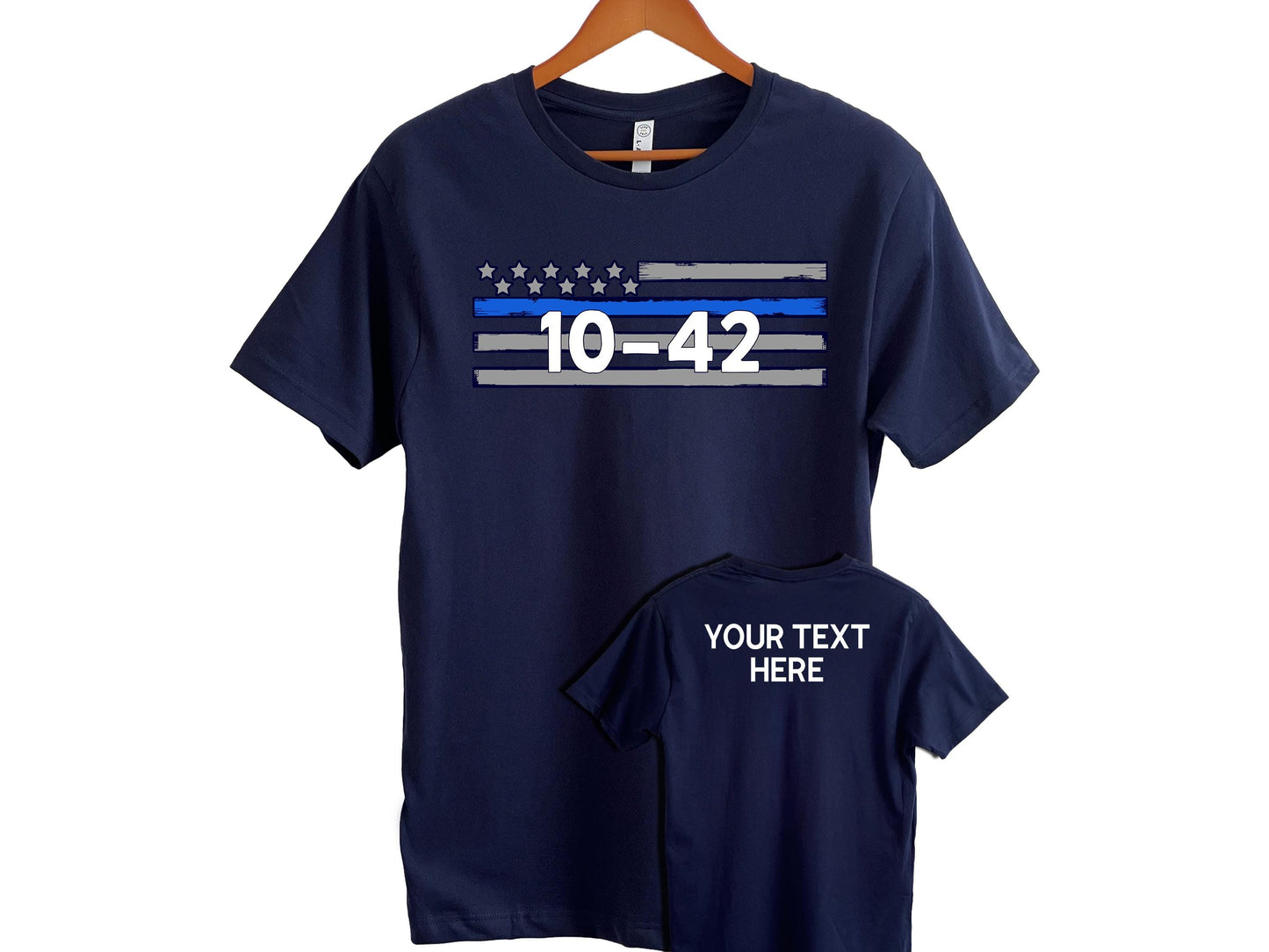 Navy blue short-sleeve t-shirt displayed on a wooden hanger, featuring a bold design on the front and customizable text on the back. The front of the shirt showcases a stylized American flag with distressed gray and blue stripes and white stars above, with the code "10-42" prominently printed in white in the center. The back of the shirt, shown in a smaller overlay image, includes placeholder text reading "YOUR TEXT HERE," indicating space for personalization.