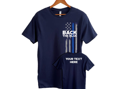 Navy blue t-shirt with a distressed vertical American flag design on the front right side, featuring a thin blue line and the bold text “BACK THE BLUE.” A smaller image shows the back of the shirt with customizable placeholder text reading “YOUR TEXT HERE.” Ideal for showing support for law enforcement.