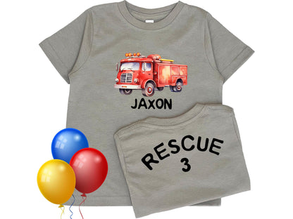 Kid's gray short sleeve T-shirt with watercolor style firetruck on the front chest and "Jaxon", representing personalized name underneath. The back of the shirt displays the number "3" representing the child's custom age.