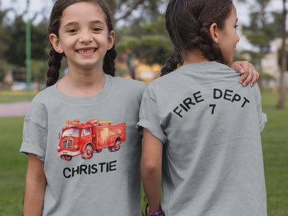 Twin girls wearing gray t-shirts, one facing forward with a red vintage watercolor firetruck printed on chest and the name Christie underneath. The other twin is facing backward with a large number 7 printed on the shirt.