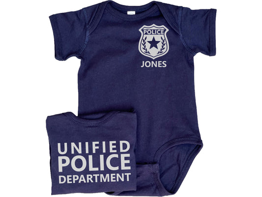Navy blue baby bodysuit with silver police badge including 5 point star and laurel leaves. Custom name underneath. Back of the bodysuit shows custom police department in silver text.