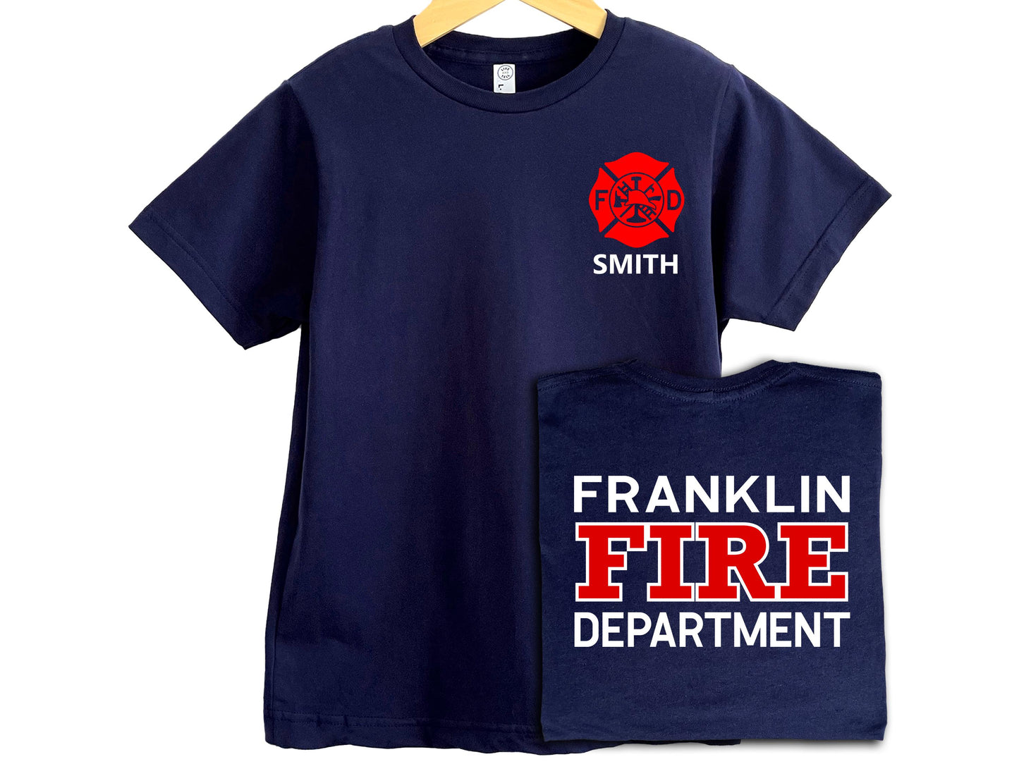 Navy blue youth sized firefighter T-shirt with red Maltese cross on left chest and personalized name underneath in white. Back of shirt features custom fire department in white and red text.