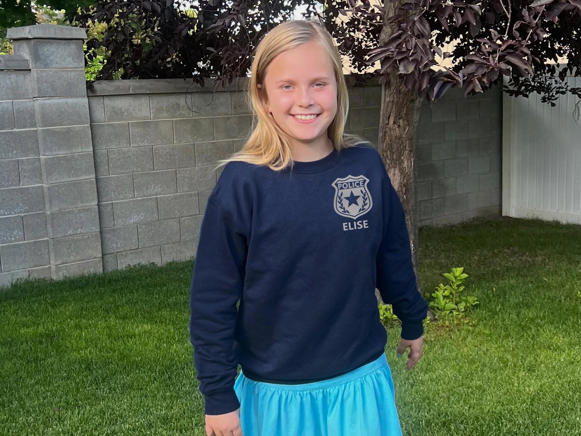 Girl wearing a navy blue sweatshirt with a silver police badge emblem on the left chest and the name 'HAILEY' in silver text.