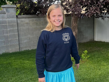 Girl wearing a navy blue sweatshirt with a silver police badge emblem on the left chest and the name 'HAILEY' in silver text.